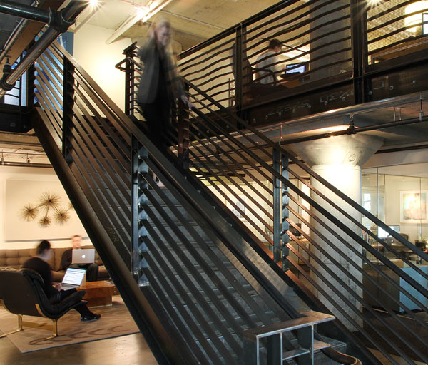 Modern staircase with people sitting beneath it and someone walking down it