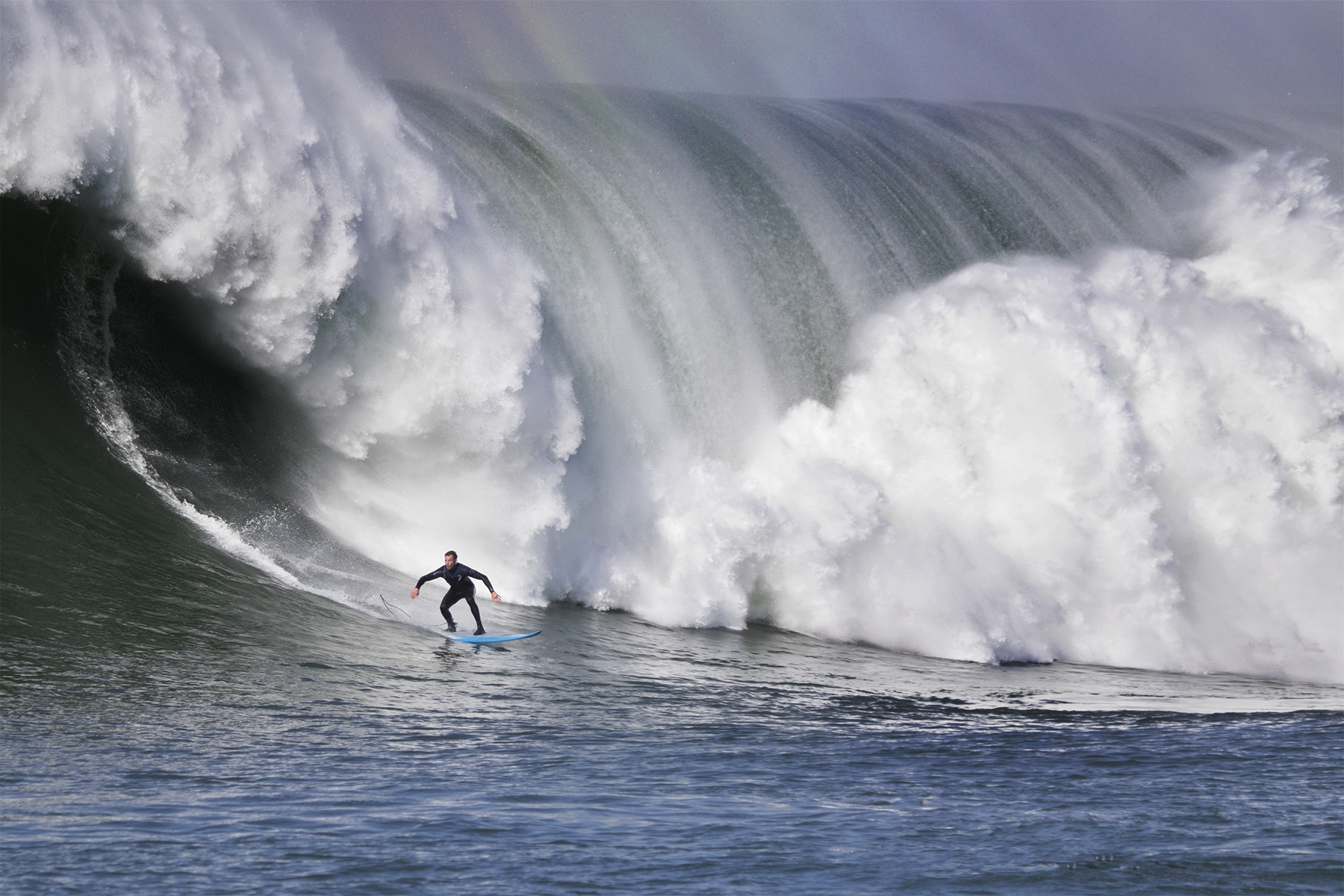 Person surfing in front of large breaking wave