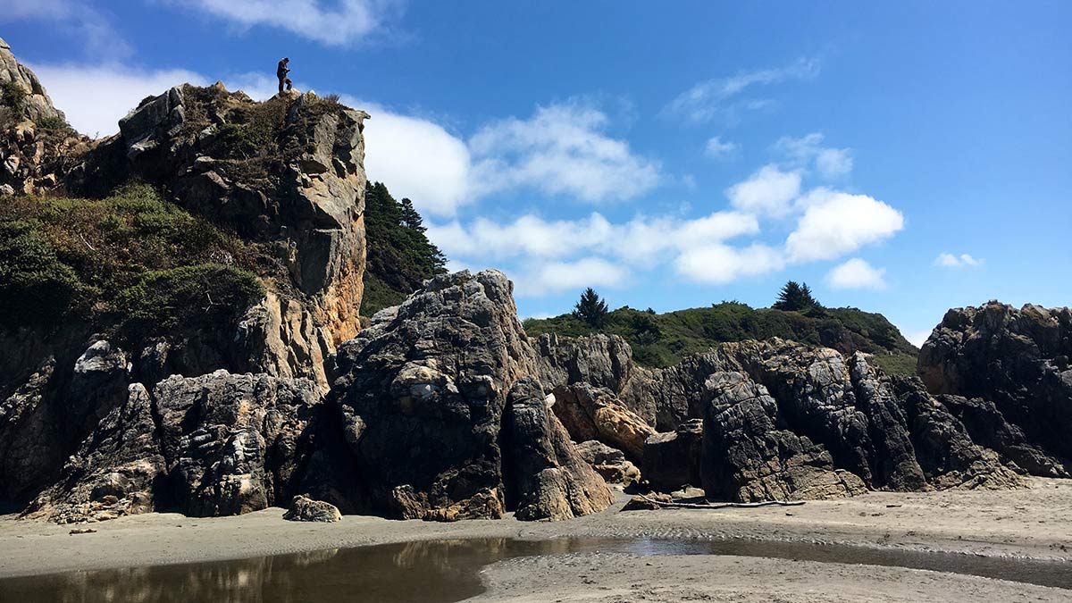 Beach with large rock outcropping with person standing on top of rocks